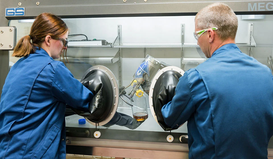 Zwei Chemikanten bei REMONDIS Industrie Service in Bramsche bei der Behandlung einer Probe in einer Handschuhbox (Glovebox).