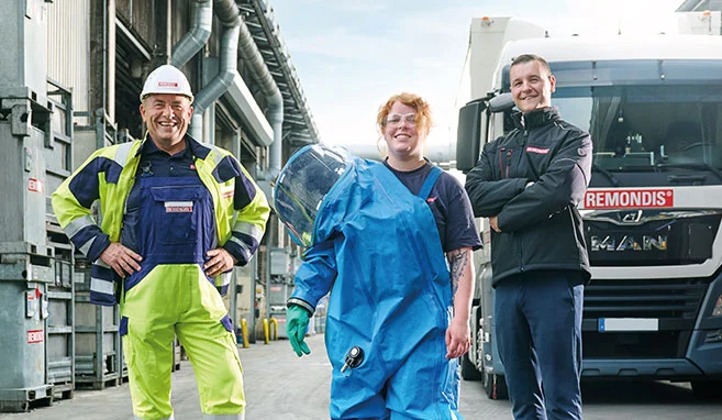 Mitarbeiter in unterschiedlicher Arbeitskleidung stehen im Industrie-Recycling-Zentrum in Bramsche und schauen Richtung Kamera. Im Hintergrund stehen verschiedene Abfallbehälter sowie ein LKW mit der Aufschrift "REMONDIS".