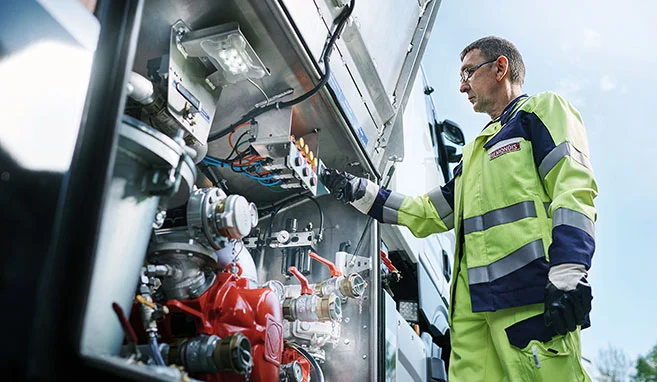 Der Fahrer des MOBIWER in Warnschutzkleidung steht seitlich am Fahrzeug an einer geöffneten Klappe und bedient einen Schalter.