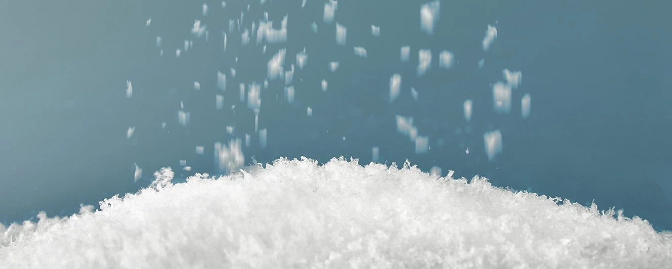 Schneeflocken vor blauem Hintergrund rieseln auf einen kleinen Schneehaufen.