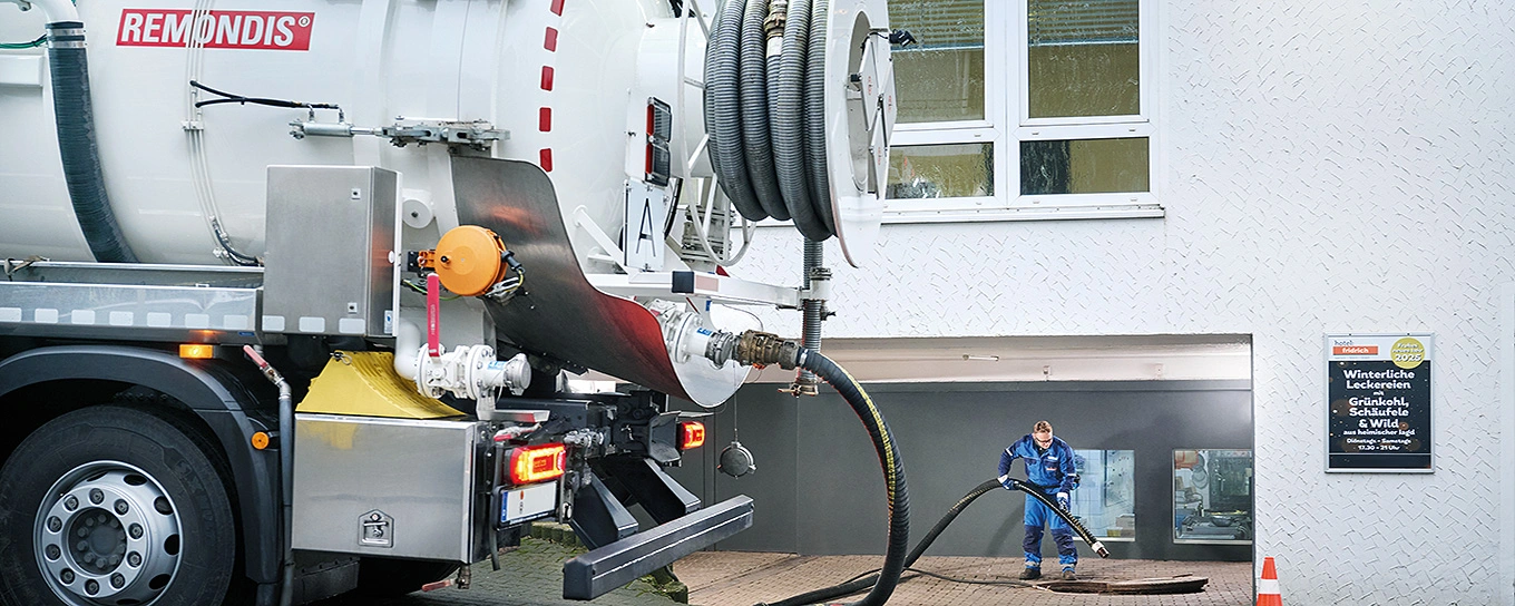 Im Vordergrund ein Saug-Druck-Tankfahrzeug und im Hintergrund ein Mitarbeiter, der einen Saugschlauch in einen Schacht hält.