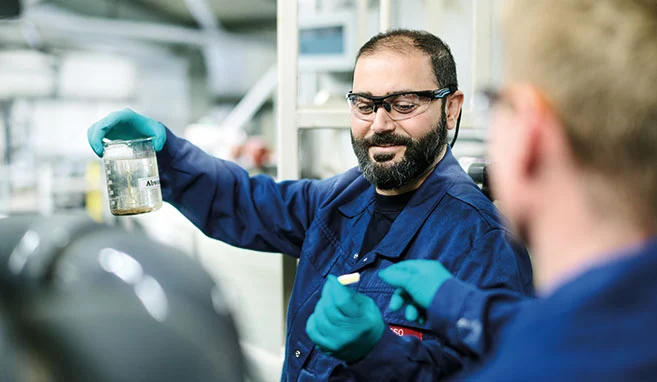 Ein Mitarbeiter hält eine Probe in der Hand und bekommt von einem Kollegen einen Teststreifen zum Testen gereicht.