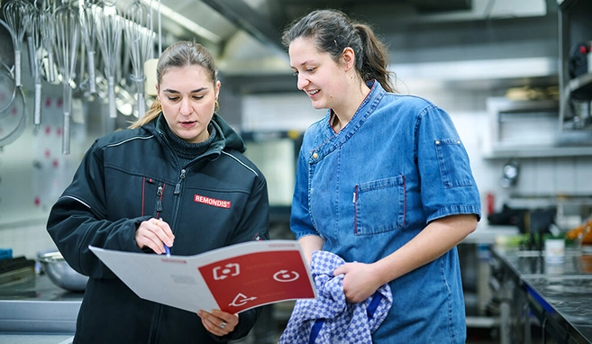 Eine Mitarbeiterin von REMONDIS Industrie Service in einer Küche einer gastronomischen Einrichtung im Gespräch mit einer Köchin
