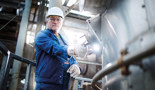 Ein Mitarbeiter steht an einer Hochtemperaturverbrennungsanlage und schaut in die Kamera