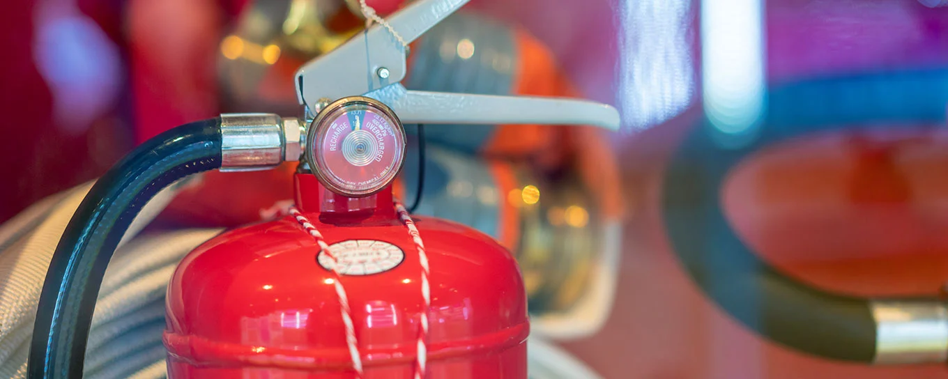 Im Vordergrund ein Feuerlöscher in Nahaufnahme mit unscharfem Hintergrund