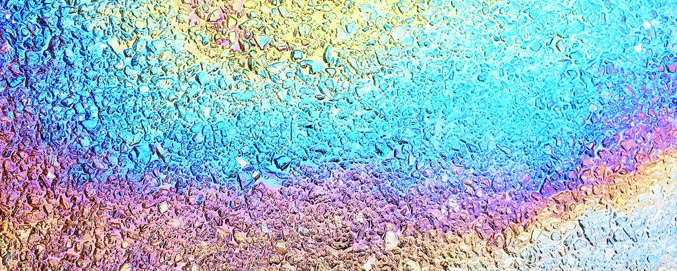 Ein Ölfleck auf Asphalt, der in Regenbogenfarben schillert